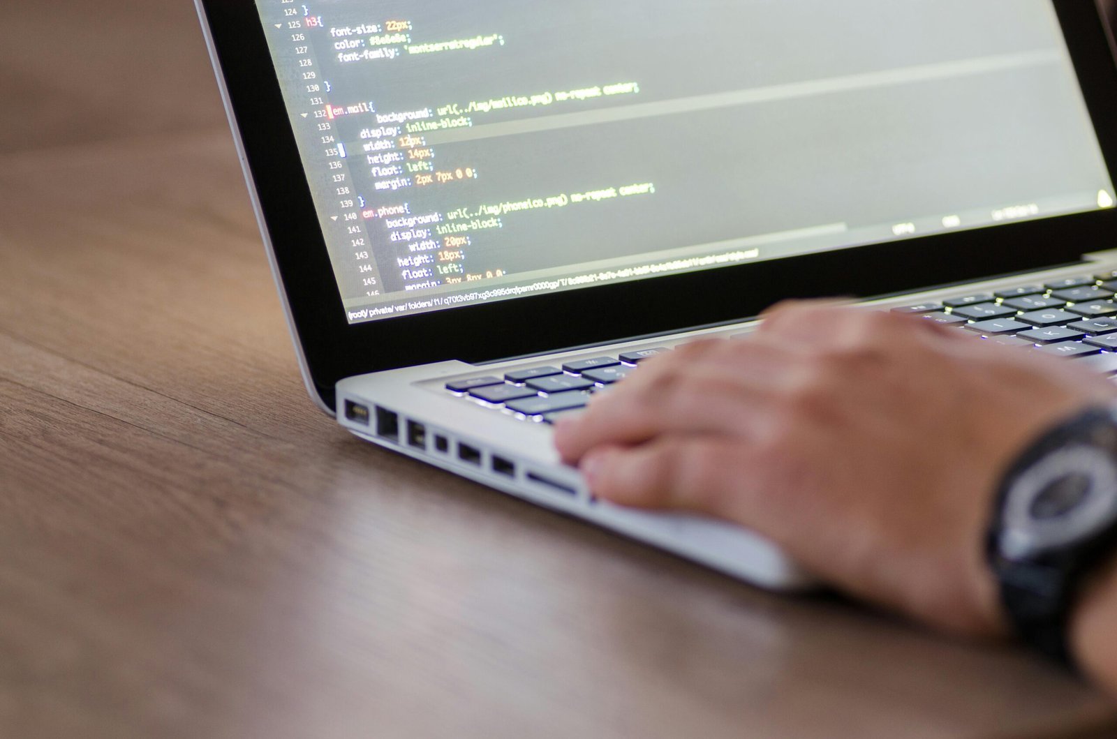Hand auf einer Laptop-Tastatur, auf dem Bildschirm ist CSS-Code geöffnet