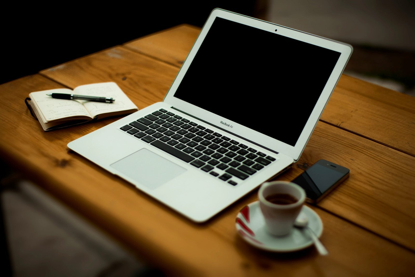 Laptop, aufgeschlagenes Notizbuch und eine Tasse Kaffee auf einem Holztisch