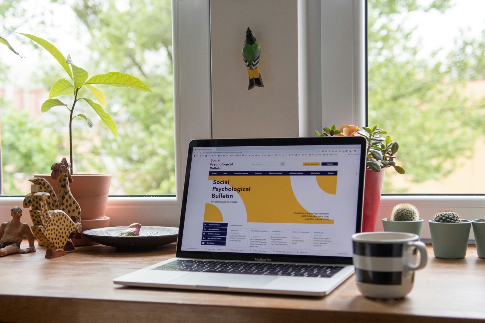 Laptop am Fenster mit geöffneter Website, daneben Zimmerpflanzen und eine Tasse